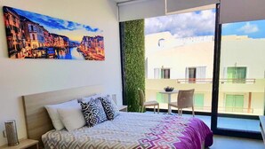 A bedroom with a bed, pillows, a bedside table, a window with a view of buildings, and a green wall. - Deluxe Studio in the best area of Playa Del Carmen by Happy Address (Playa del Carmen)