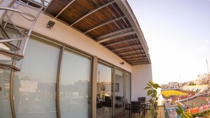 Een balkon met een houten vloer, grote schuifdeuren en uitzicht op een sportveld.