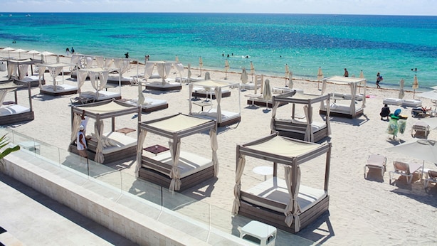 Un resort frente a la playa con varias cabañas sobre el agua, una playa de arena y una vista despejada del mar turquesa.