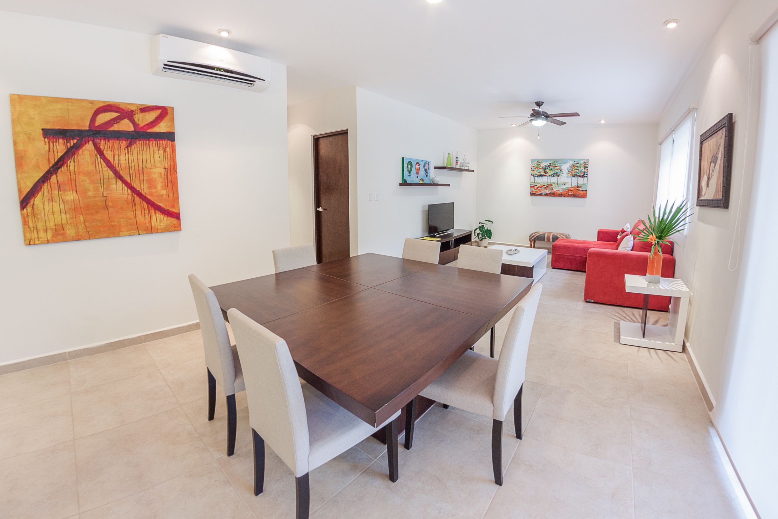A modern dining area with a large wooden table, white chairs, and a red sofa.