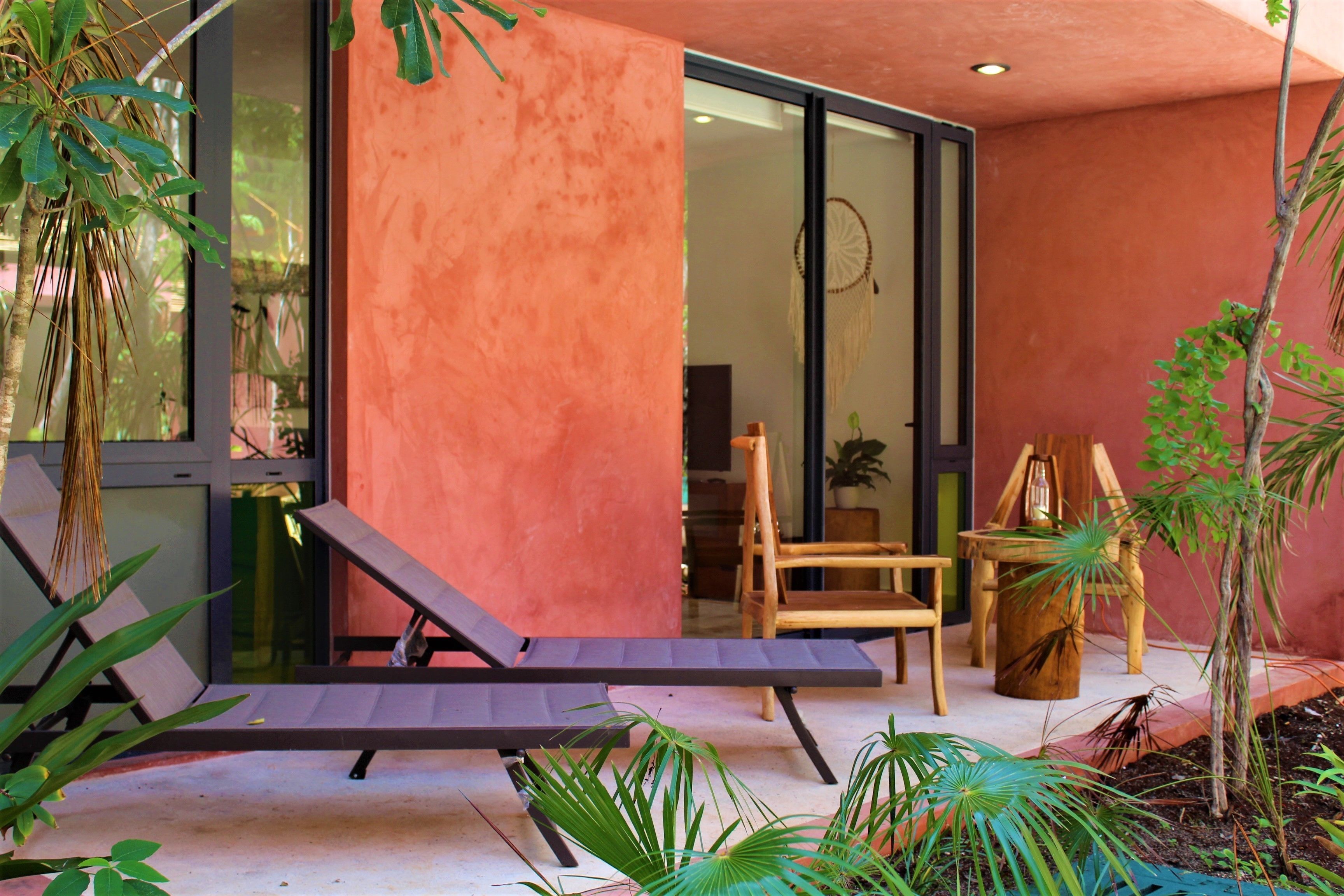 A modern outdoor seating area with a lounge chair and a wooden table, surrounded by potted plants.