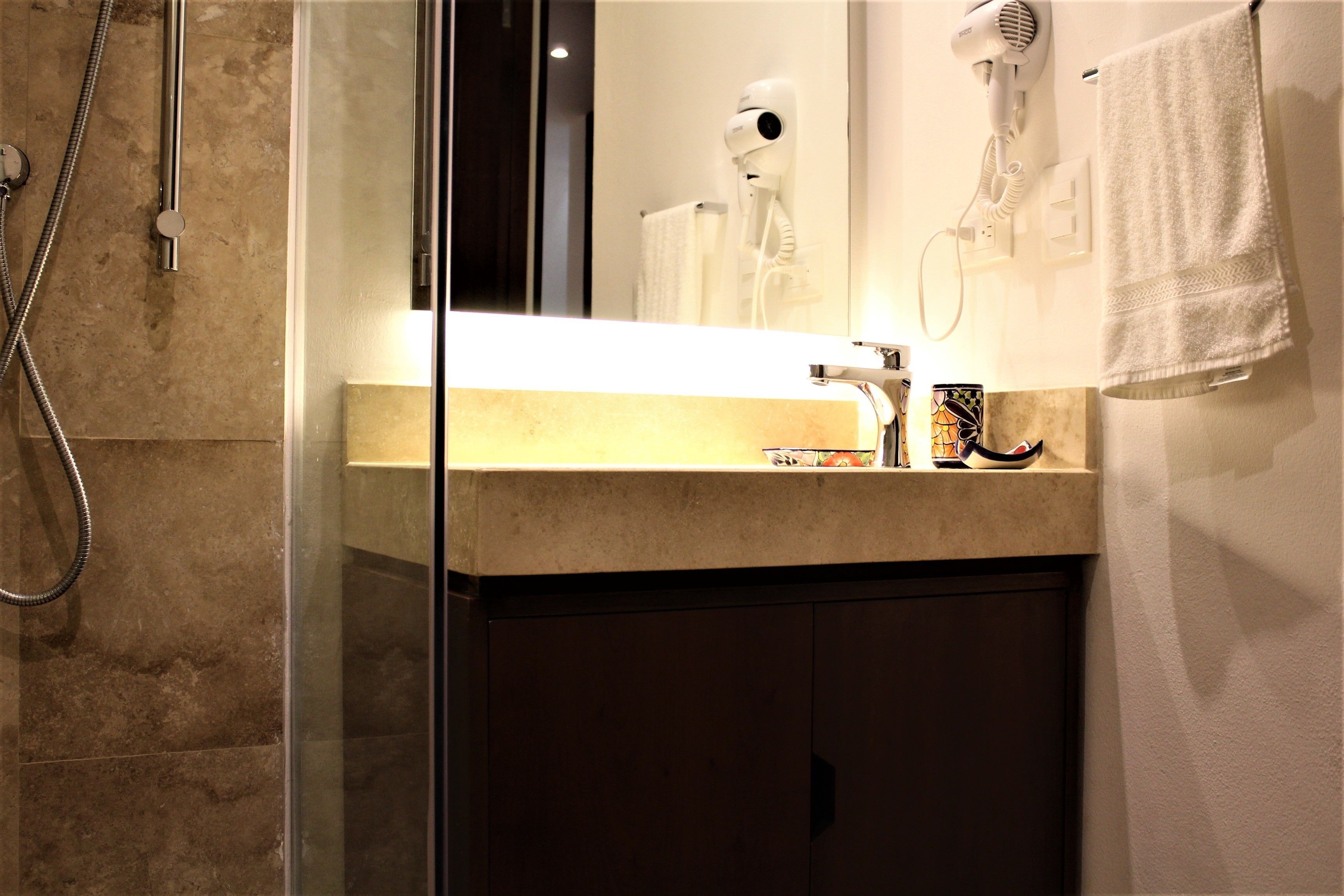 A bathroom with a glass shower enclosure, a marble countertop, a hairdryer, and a towel hanging on the wall.