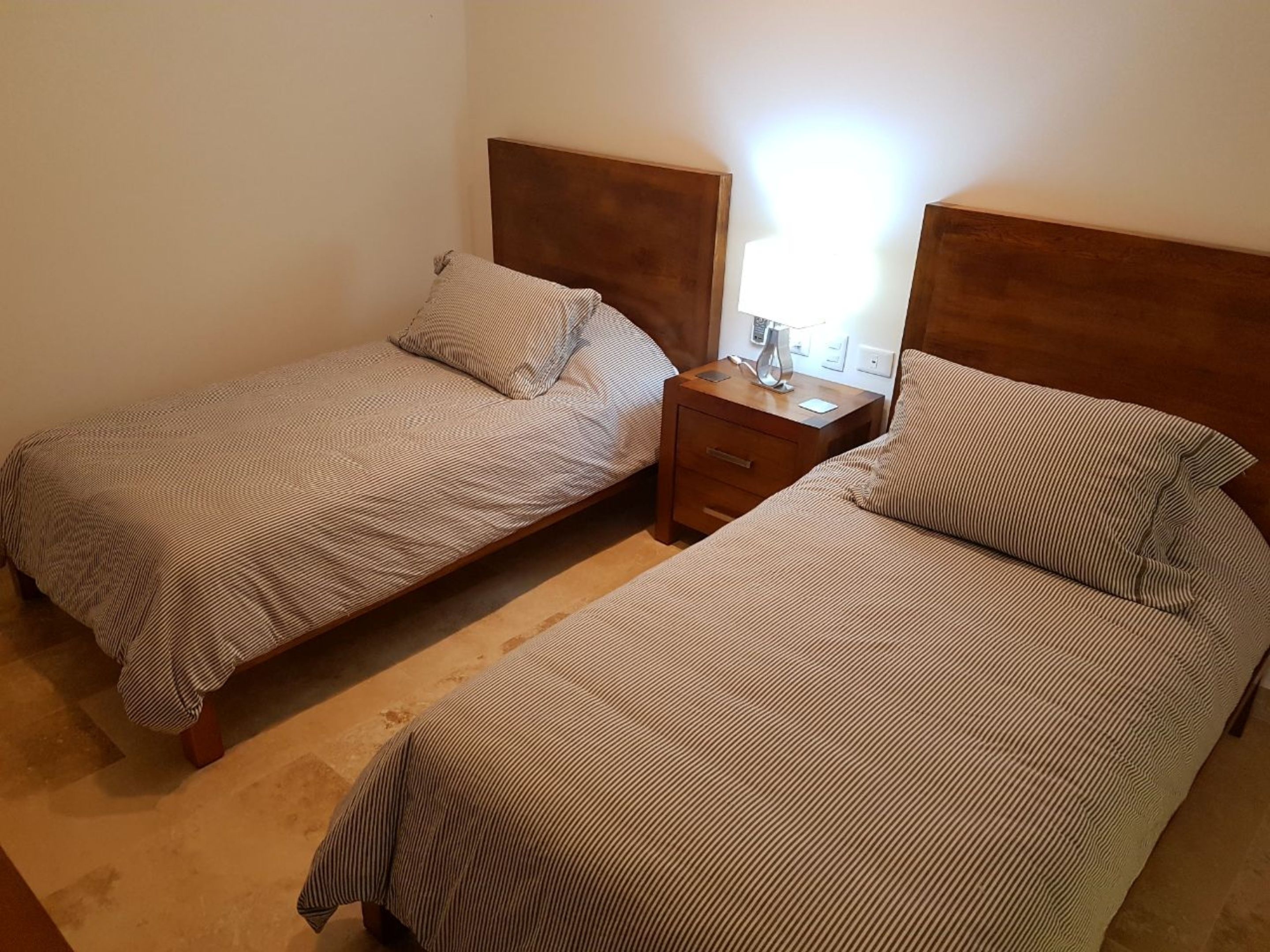 Una habitación con dos camas individuales, cada una con cabecera de madera y una mesita de noche con lámpara.