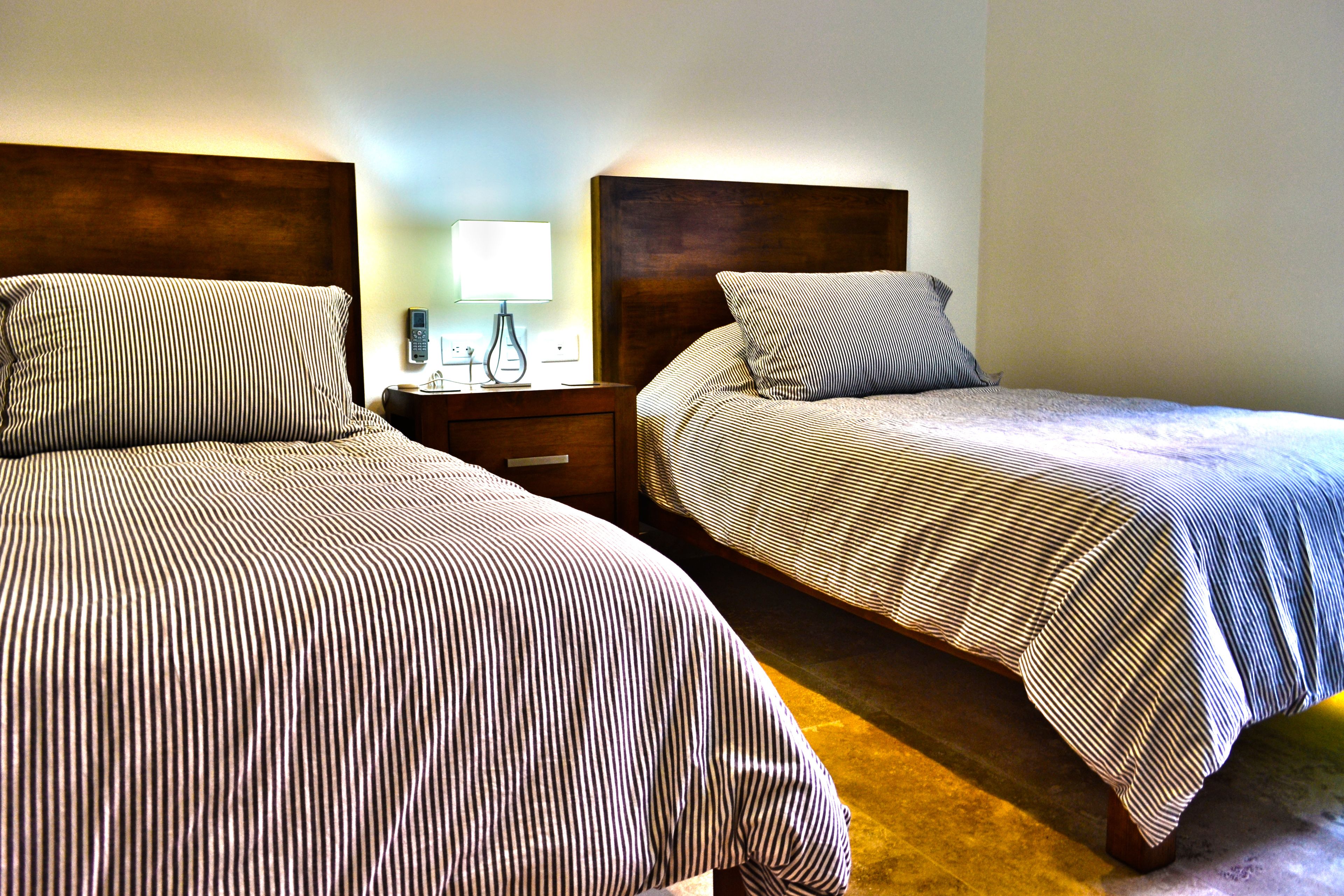 Two single beds with striped bedding, a bedside table with a lamp, and a nightstand with a phone.