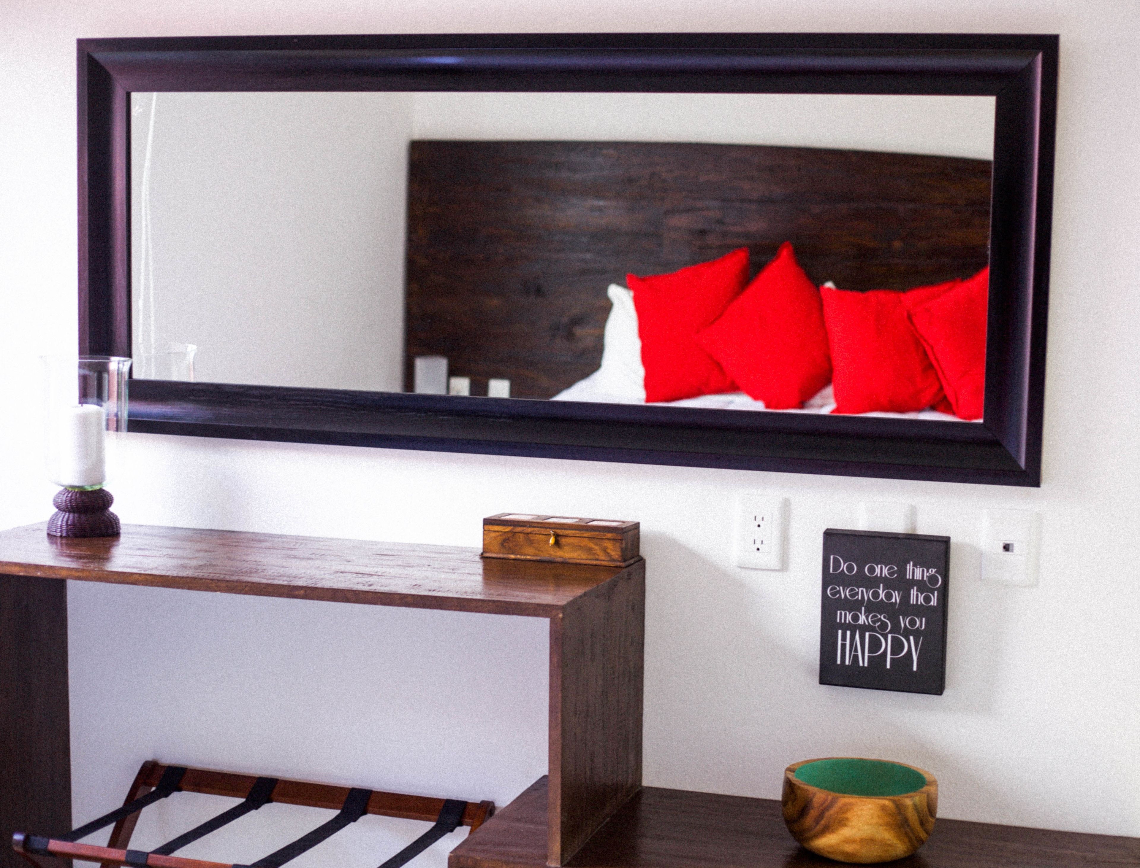 Un miroir avec un cadre foncé, une table de chevet sur laquelle se trouve une petite boîte en bois, un bol vert et une citation inspirante accrochée au mur.