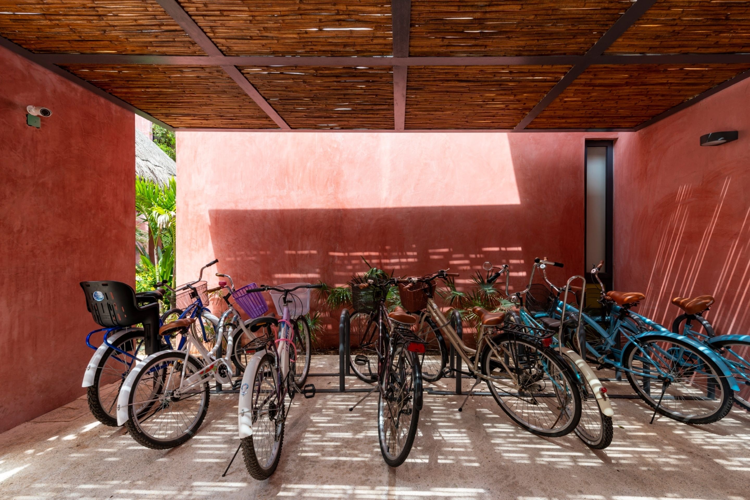 A covered bike parking area with multiple bicycles and a red wall.
