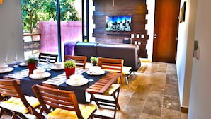 Un coin repas avec une longue table dressée pour six personnes, des chaises en bois et une vue sur l’extérieur.