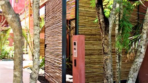 A bamboo wall structure with a small red panel, surrounded by trees and plants. - Amazing 2BR condo in wonderful location of Tulum by Happy Address (Tulum)