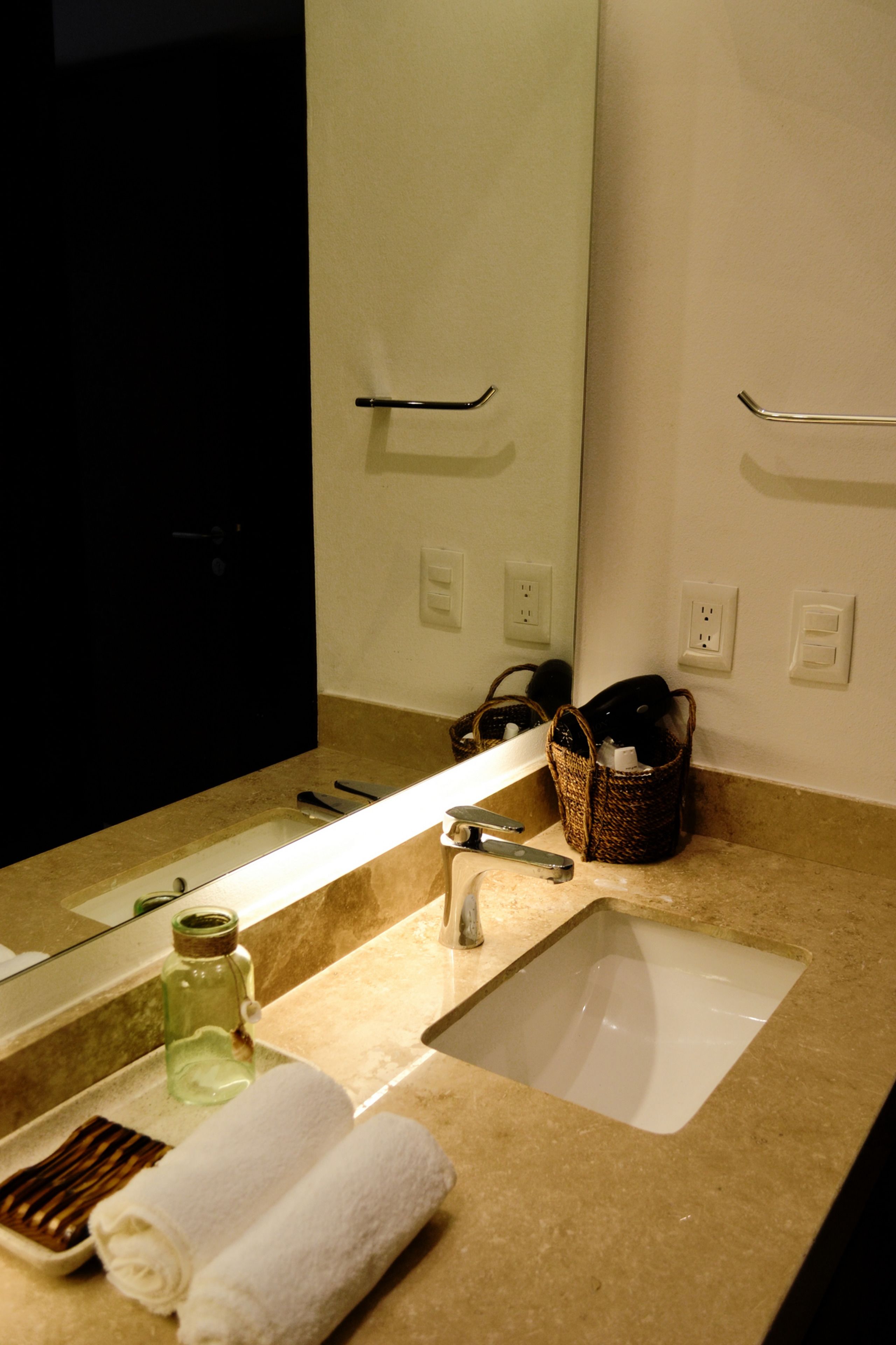 A bathroom with a sink, mirror, towel, and a basket on the counter.