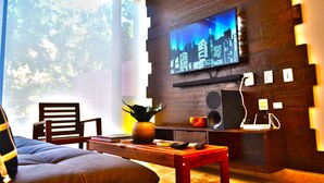 A modern living room with a large flat-screen TV mounted on a wooden wall, a comfortable sofa, a coffee table, and a small side table with a plant. - Amazing 2BR condo in wonderful location of Tulum by Happy Address (Tulum)