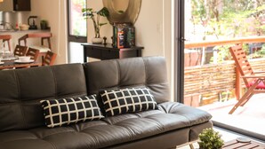 A modern living room with a leather sofa, a coffee table, and a dining area visible through a glass door. - Lavish 1 BR Condo for 2 people with private terrace by Happy Address (Tulum)