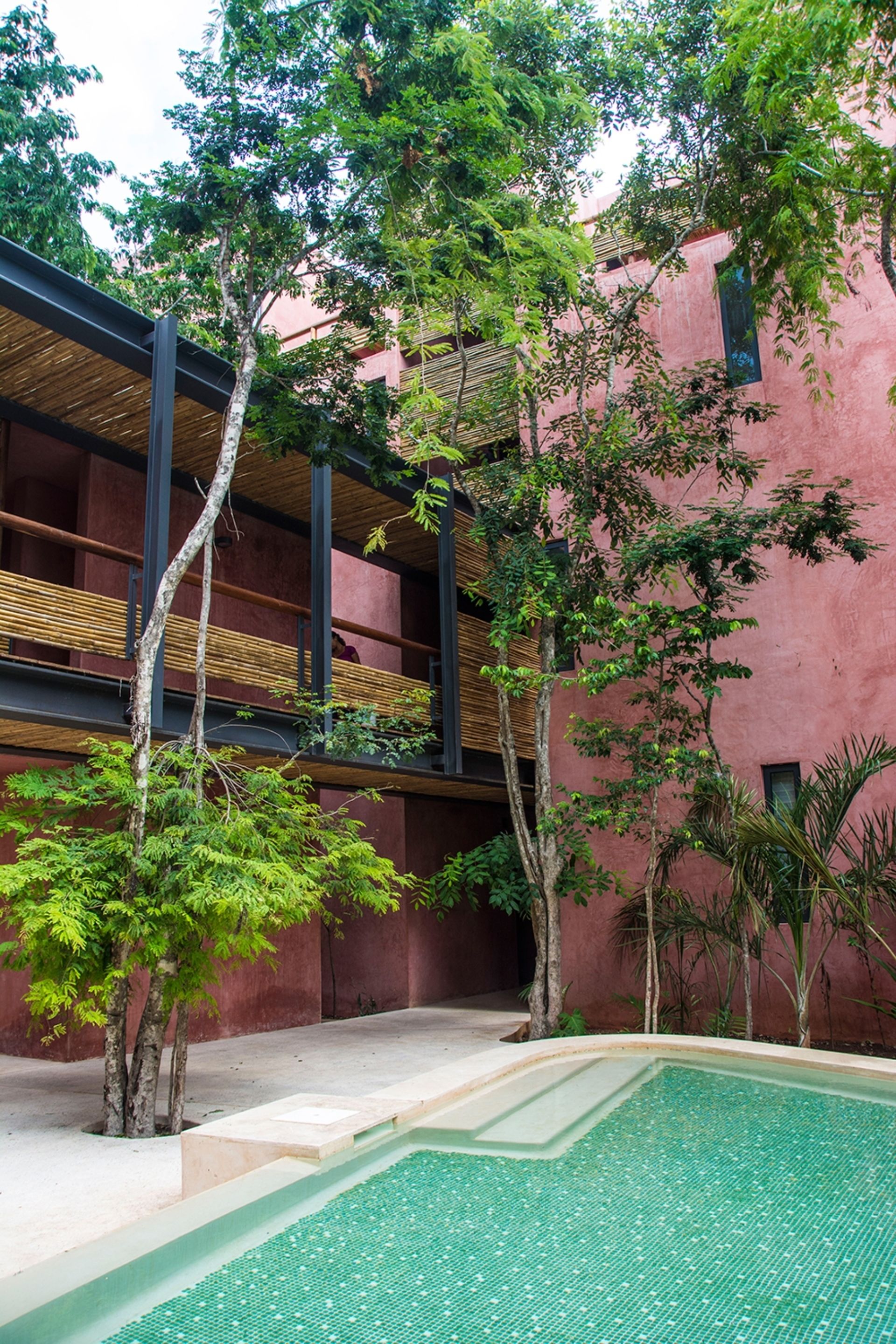 A courtyard with a swimming pool, trees, and a building with a pink facade and wooden balconies.