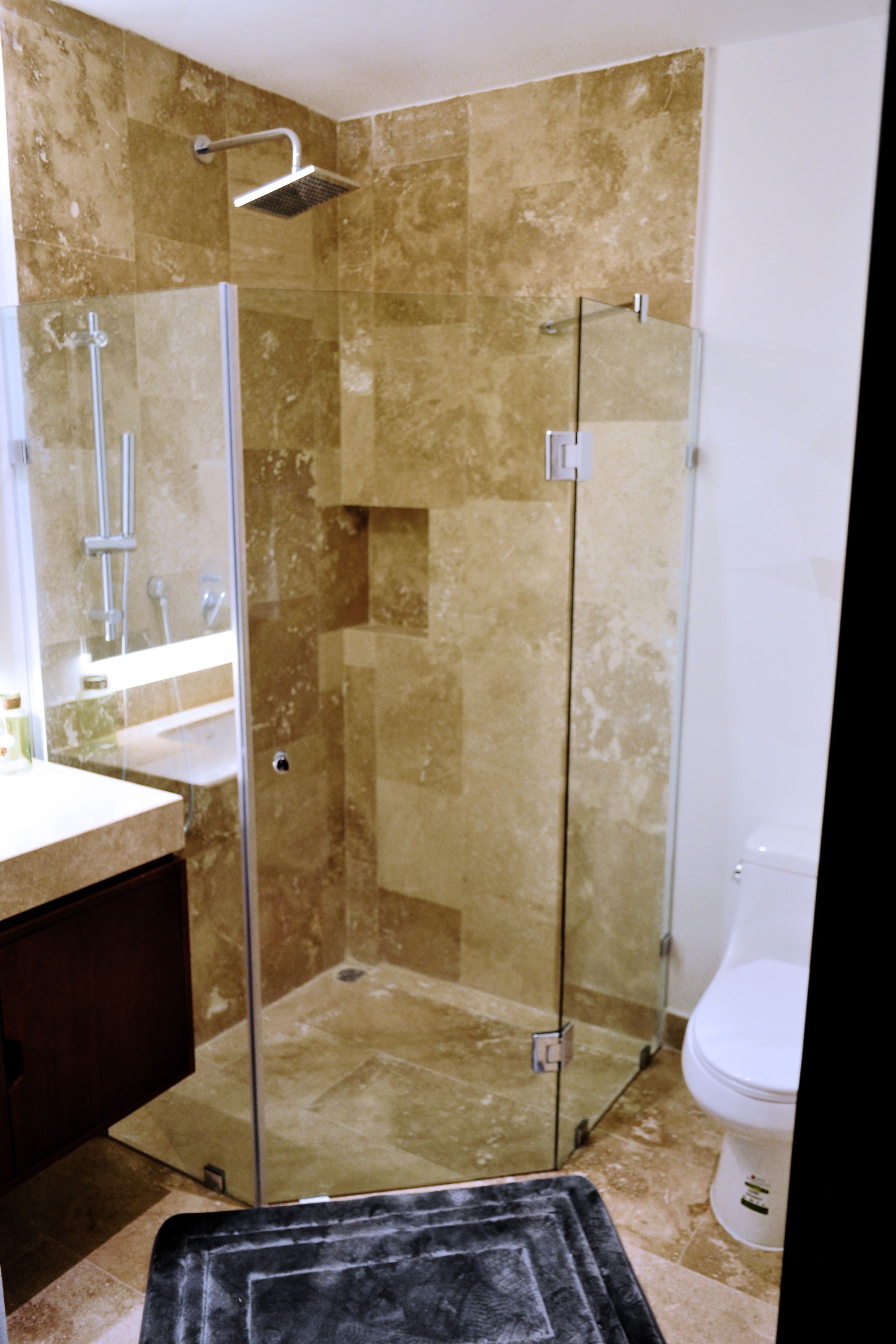 A glass-enclosed shower stall with a handheld showerhead, a sink with a mirror, and a toilet.