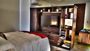 A bedroom with a large bed, a wooden wardrobe with a TV, and a small table with a lamp. - Lavish 1 BR Condo for 2 people with private terrace by Happy Address (Tulum)