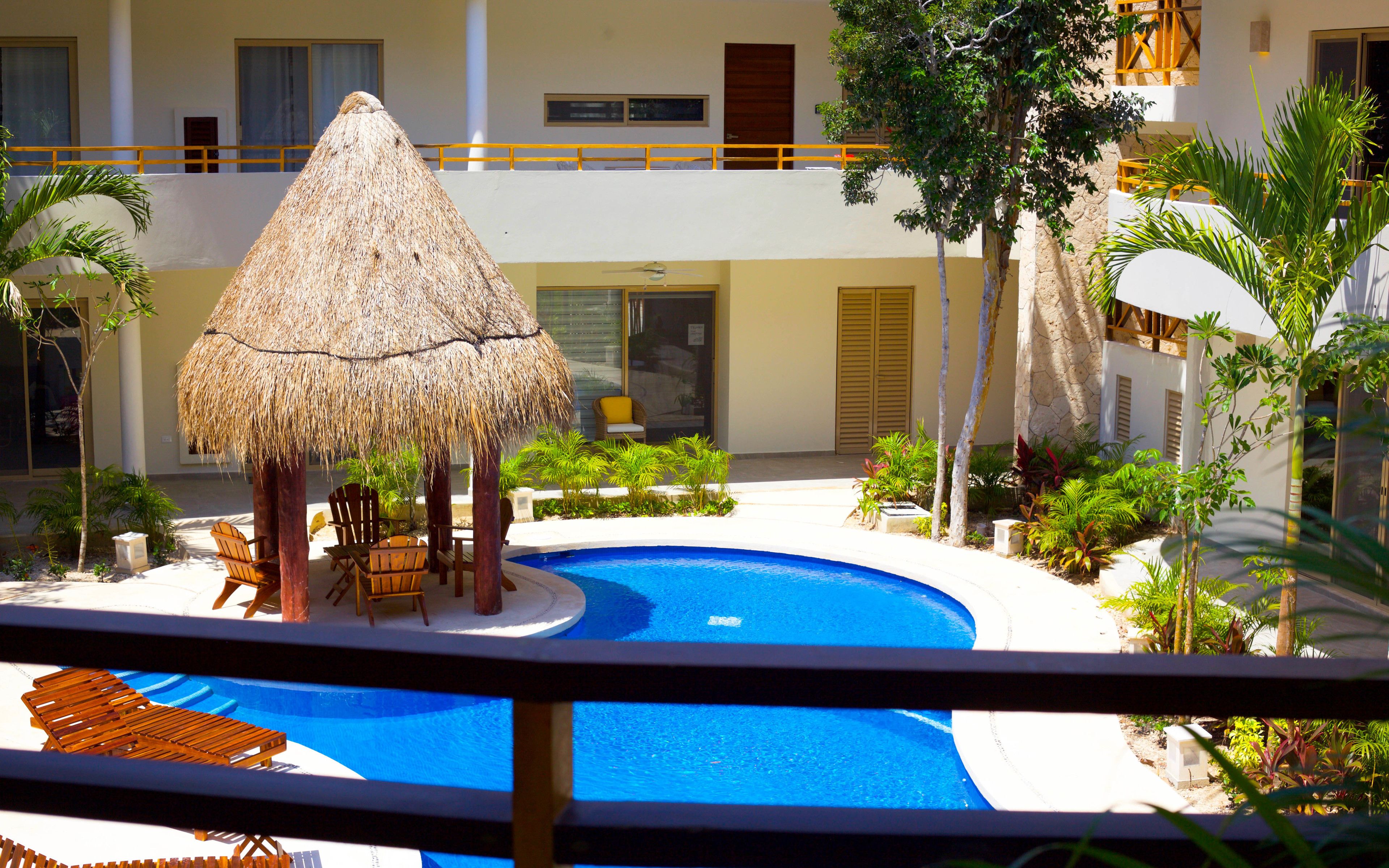 A pool area with a thatched umbrella, lounge chairs, and tropical plants.