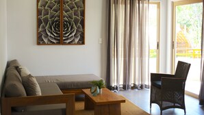 Un salon comprenant un canapé, une table basse en bois, un fauteuil en osier et une grande fenêtre avec des rideaux.
