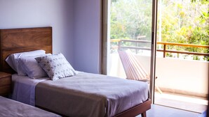 Une chambre à coucher avec une tête de lit en bois, un lit agrémenté d’un coussin à motifs et une vue sur un balcon doté d’une balustrade.