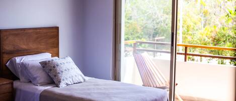 Un dormitorio con cabecera de madera, una cama con almohada estampada y vistas a un balcón con barandilla.