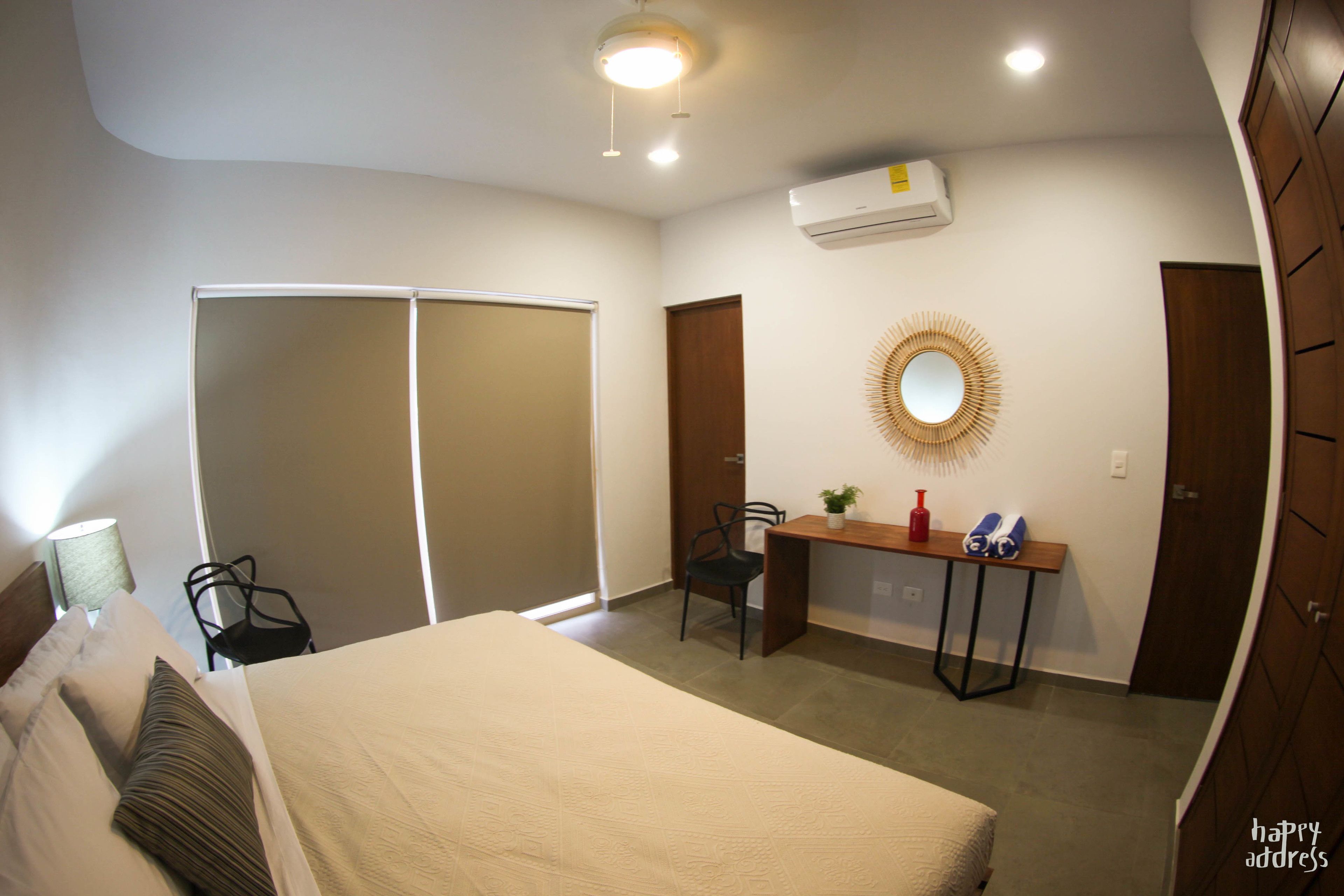 A hotel room with a bed, a desk with a chair, a mirror, and a wardrobe.