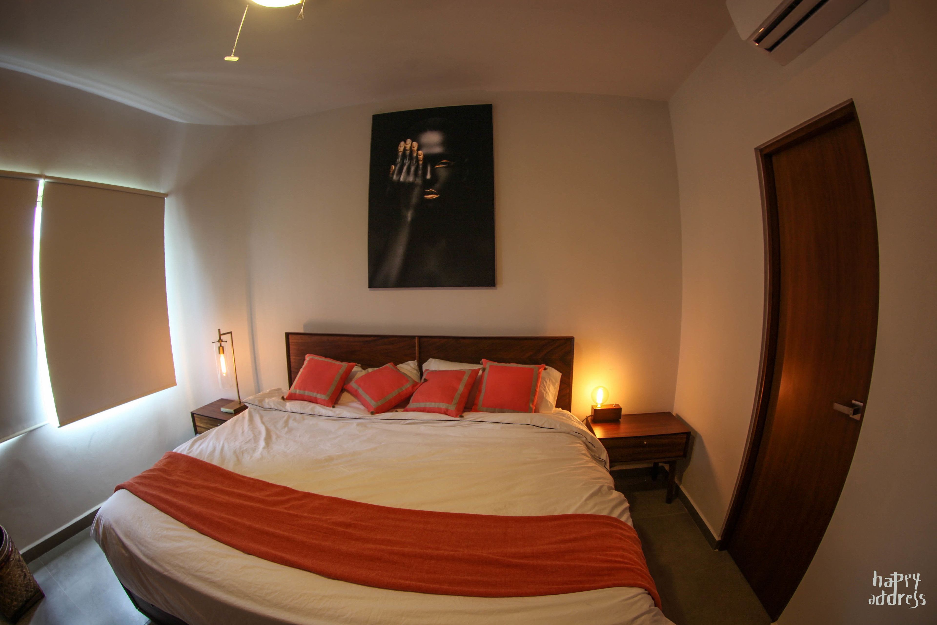 A hotel room with a large bed, a nightstand, a bedside lamp, a window with curtains, and a door.