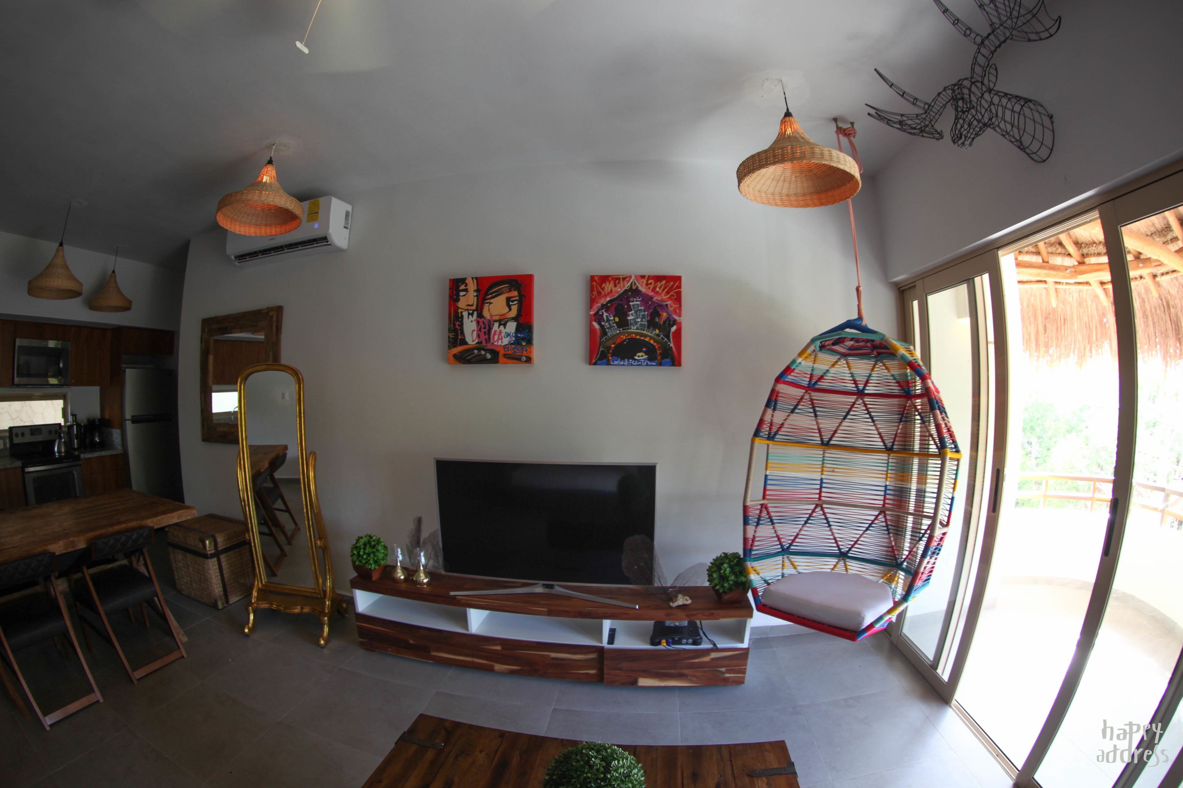 Una sala de estar moderna con un televisor de pantalla plana grande, muebles de madera y una silla colgante colorida.