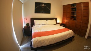 Un dormitorio con una cama grande, una mesita de noche, una lámpara de pared, un ventilador de techo y un armario de madera.