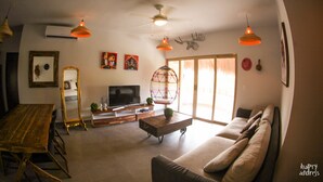 Amplia sala de estar con mesa de comedor de madera, sofá, televisor y ventilador de techo.