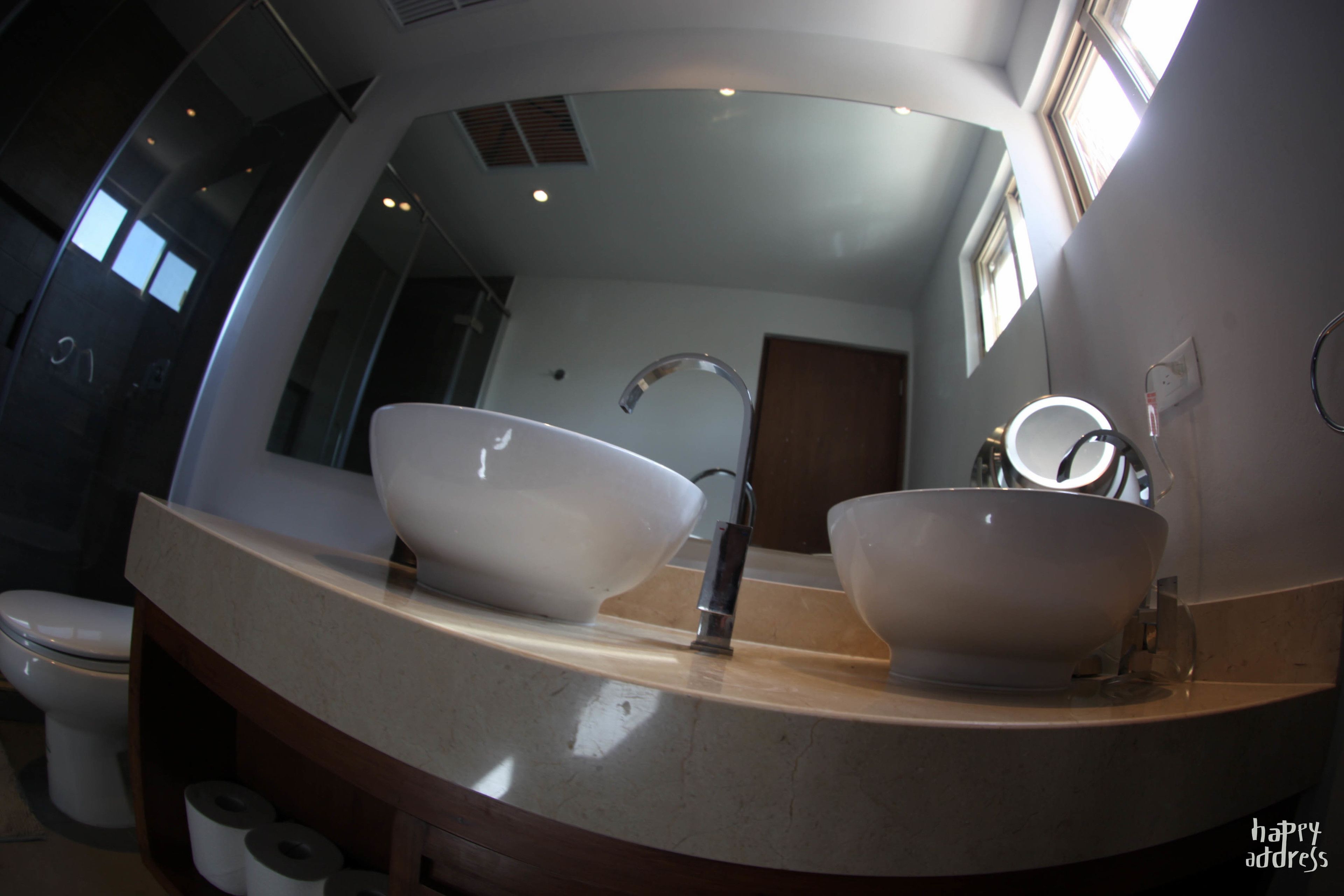 A bathroom with a large mirror, two sinks, a toilet, and a roll of toilet paper.