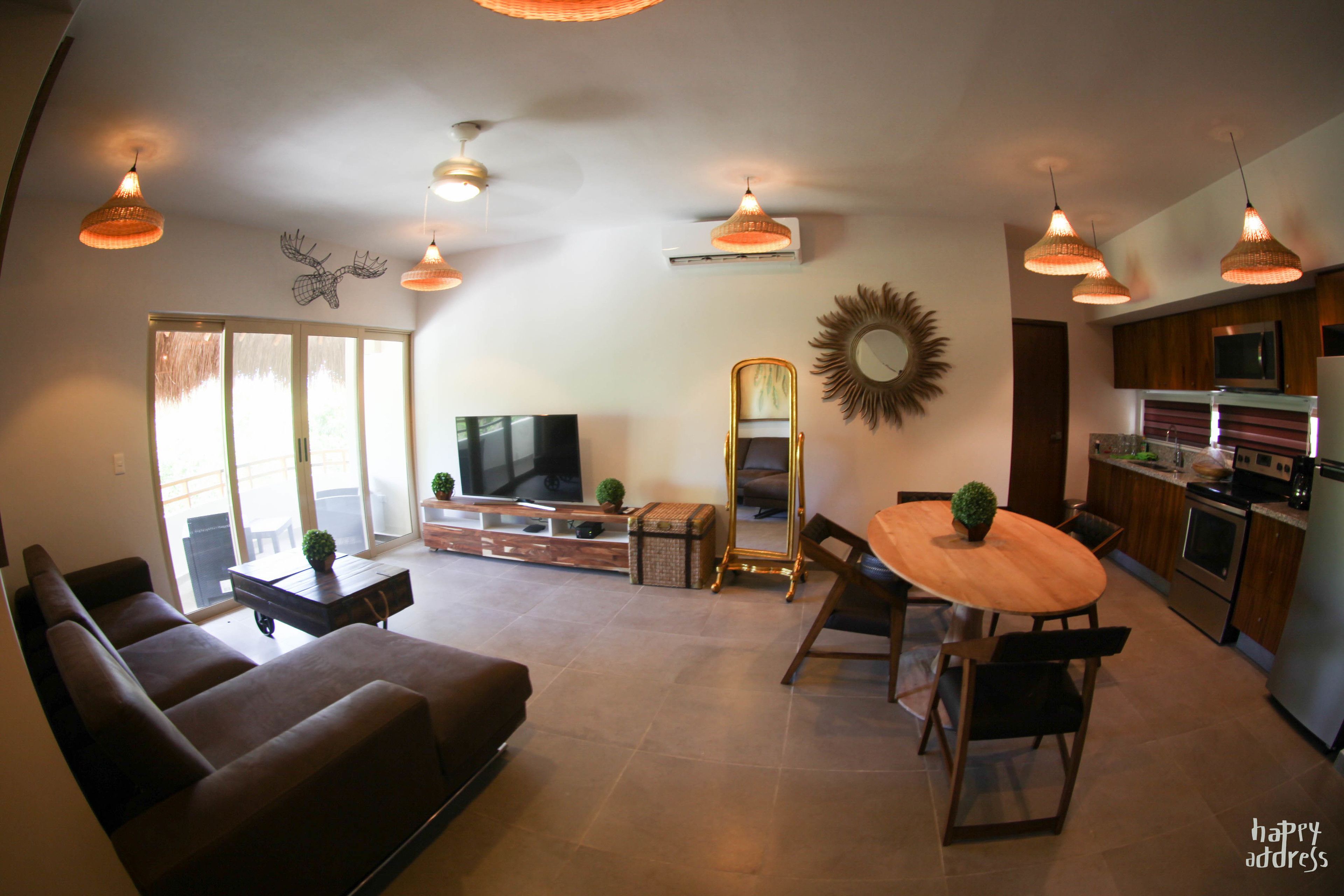 A modern living room with a sofa, a dining table with chairs, a TV, and a kitchen area with appliances.