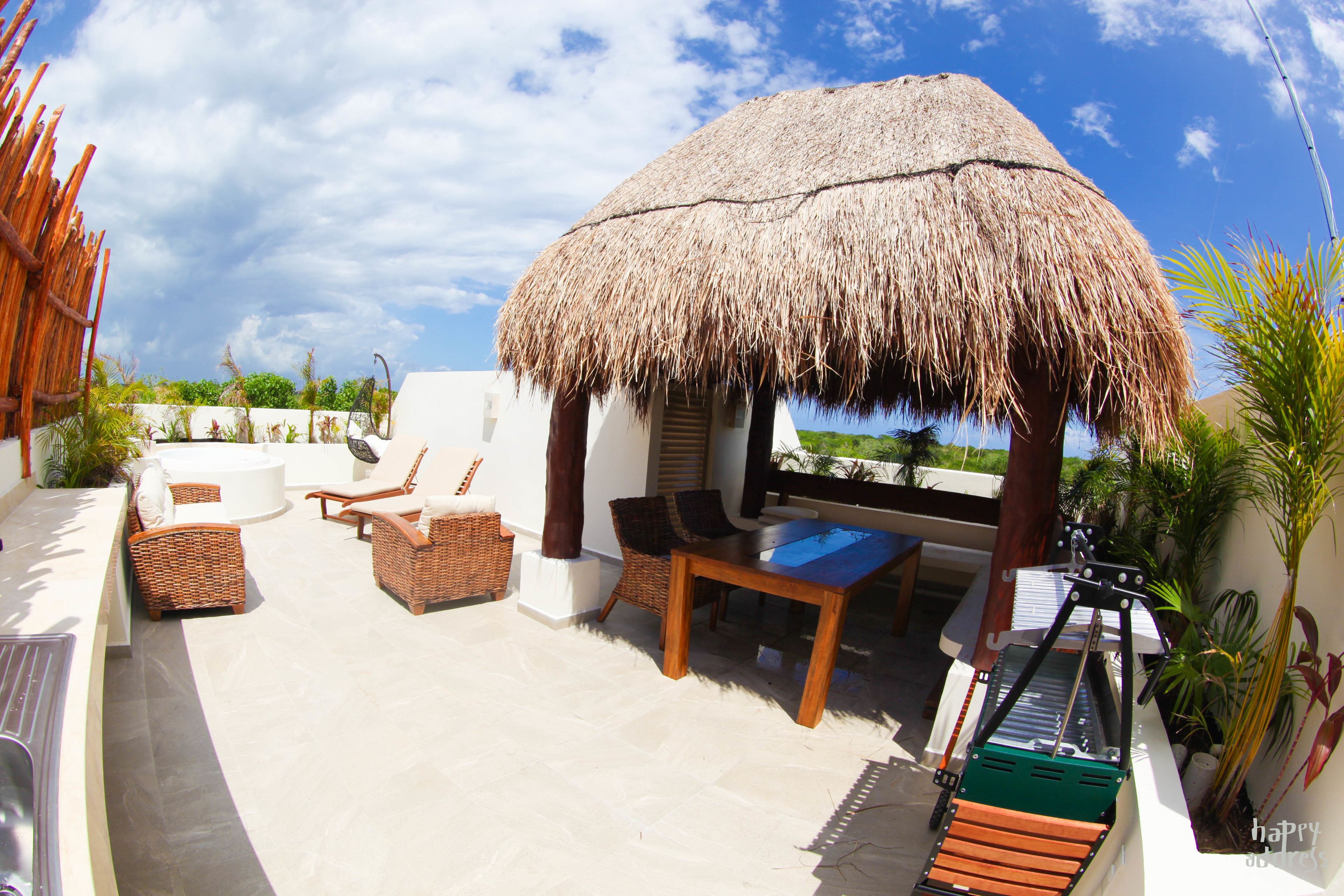 A rooftop terrace with a thatched roof, wicker furniture, and a pool table.