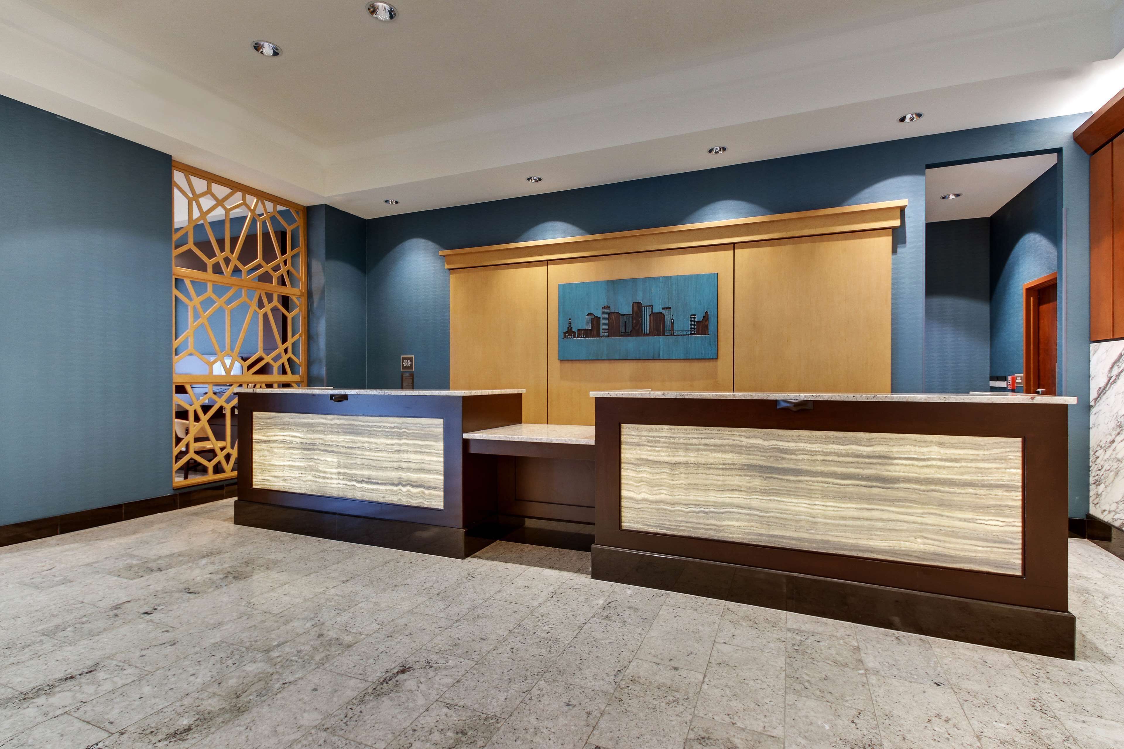 Un área de recepción con mostrador, un cuadro de paisaje urbano y un panel decorativo de madera.
