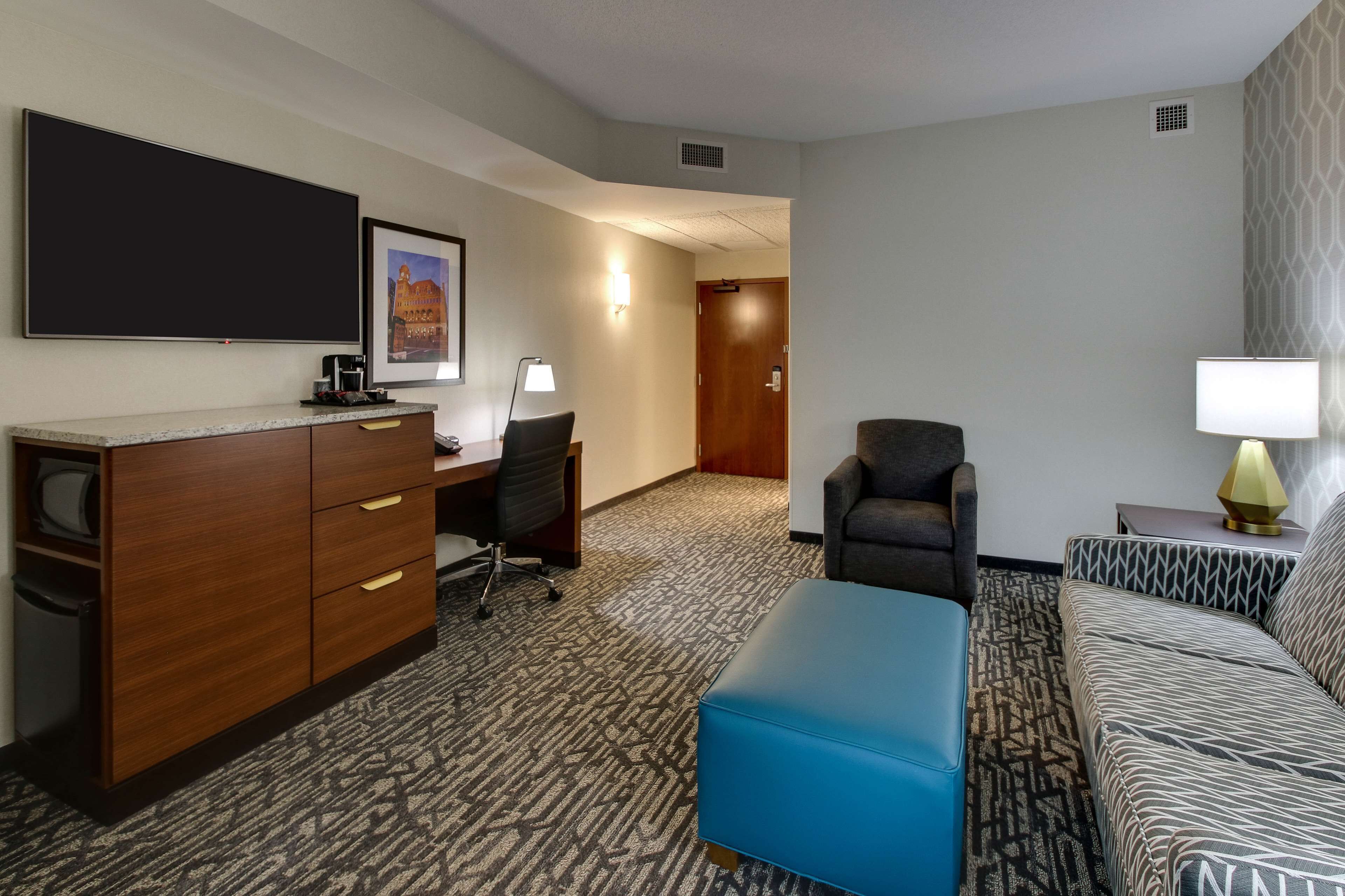 Een hotelkamer met een bureau, stoel, bank en voetenbank.