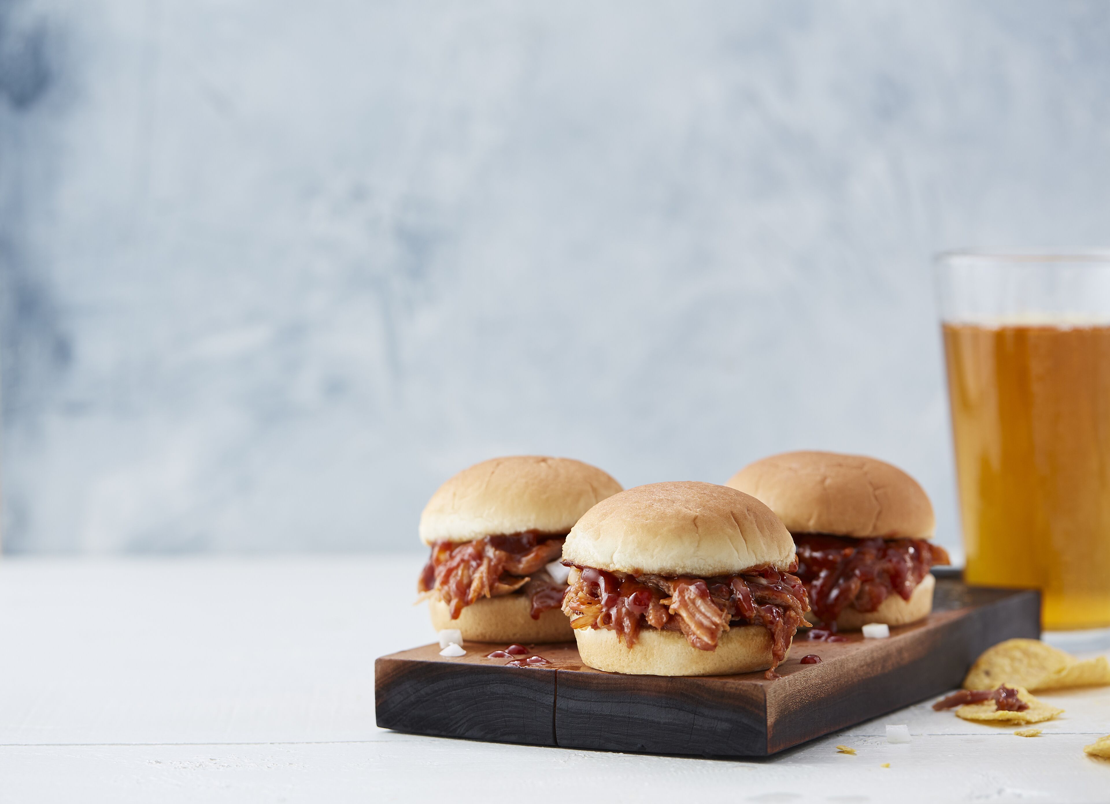 Two sandwiches on a wooden board with a glass of beer in the background.