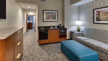 Une chambre d’hôtel équipée d’une kitchenette, d’un canapé, d’un banc et d’un tableau encadré au mur.