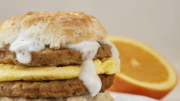 A breakfast sandwich on a plate with a slice of orange in the background.