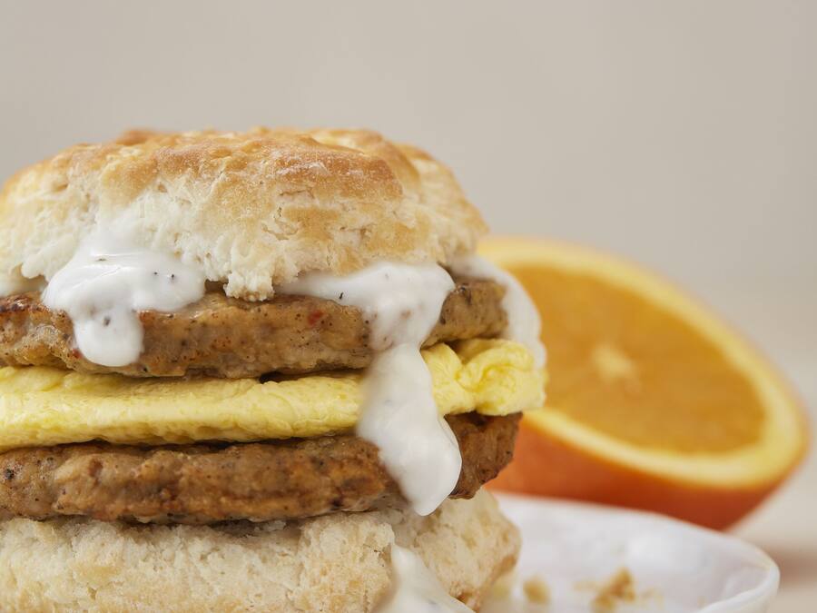A breakfast sandwich on a plate with a slice of orange in the background.