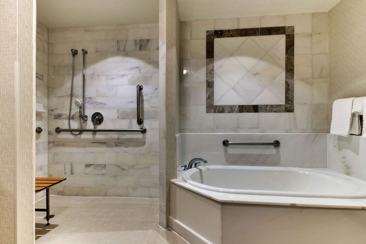 A modern bathroom with a walk-in shower, grab bars, a bathtub, and a towel rack.