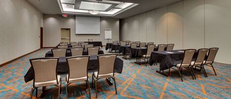 A conference room with tables and chairs, a projector screen, and a carpeted floor.
