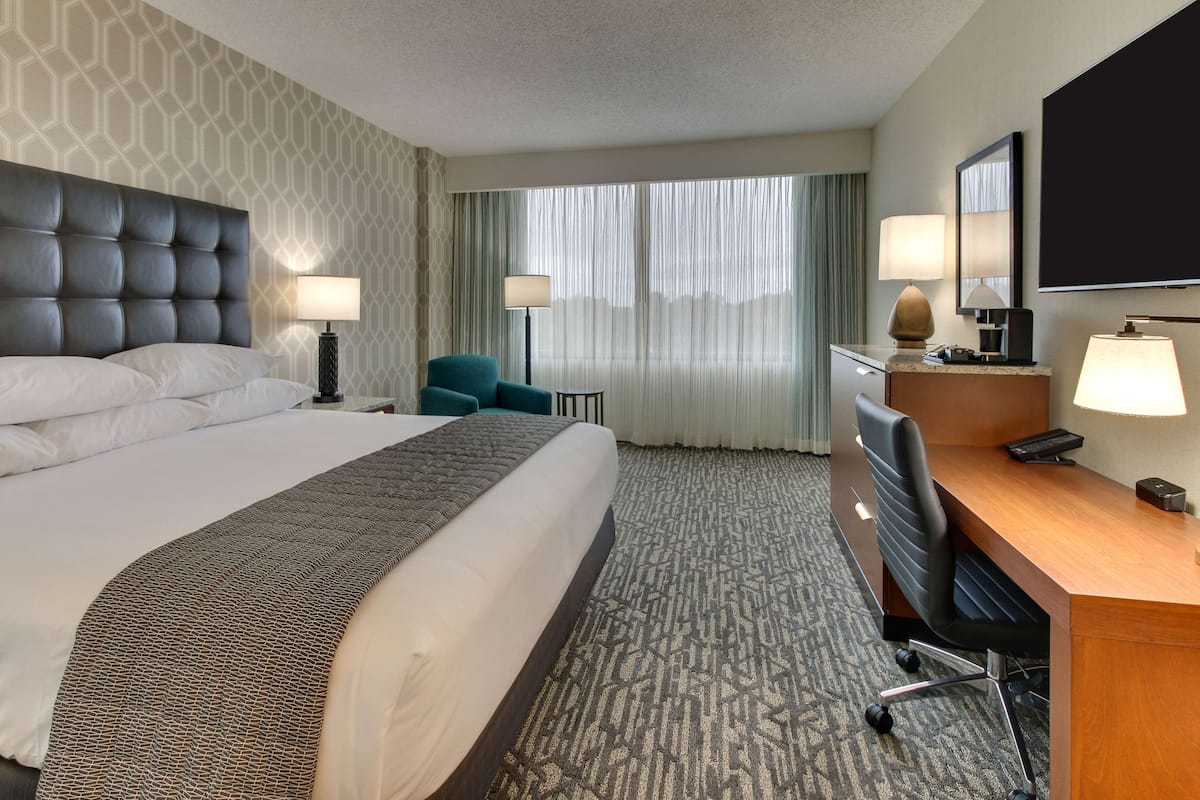 A hotel room with a large bed, a desk with a chair, a television, and two lamps.