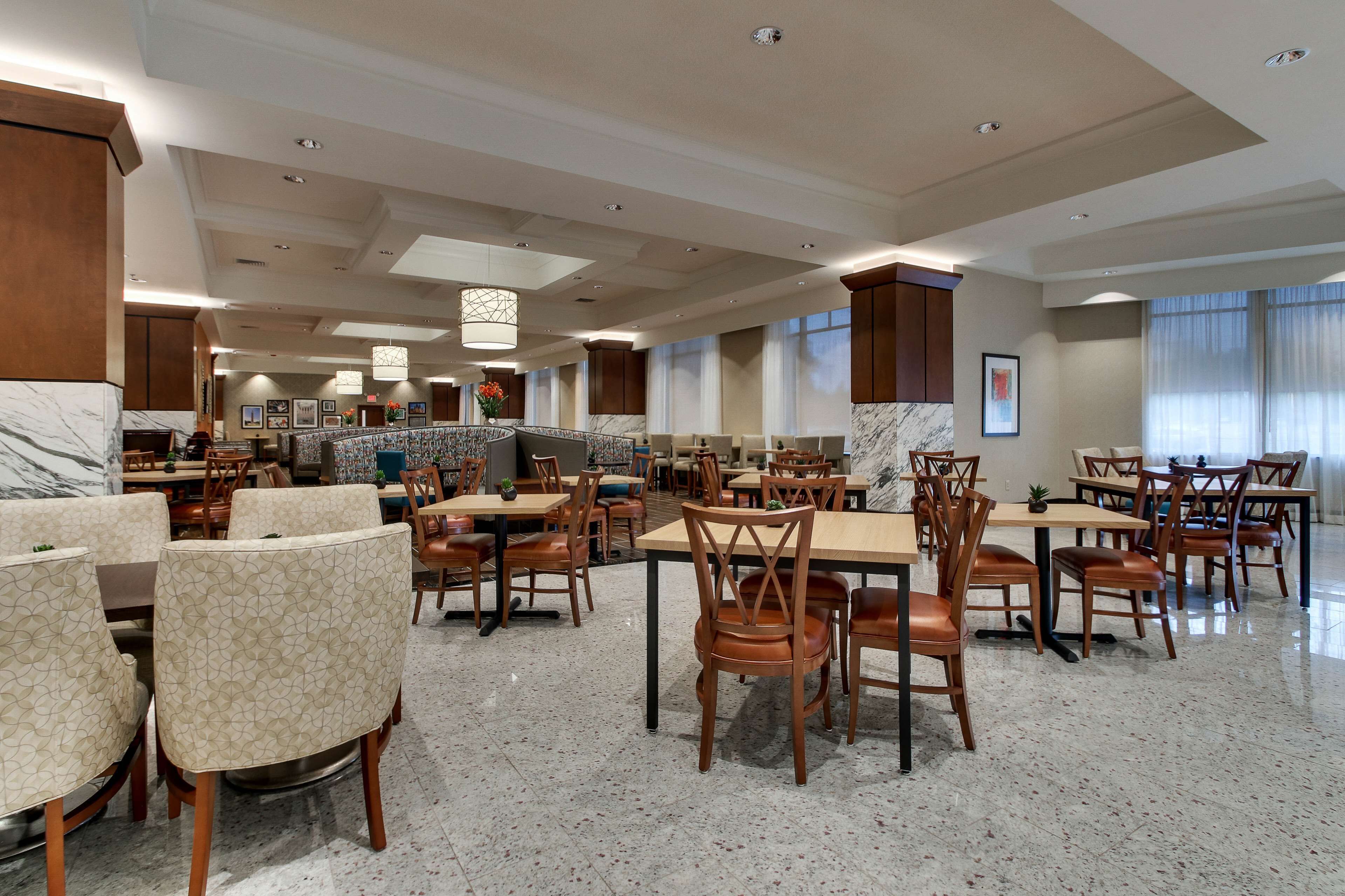 A spacious hotel dining area with multiple tables and chairs, marble flooring, and large windows.