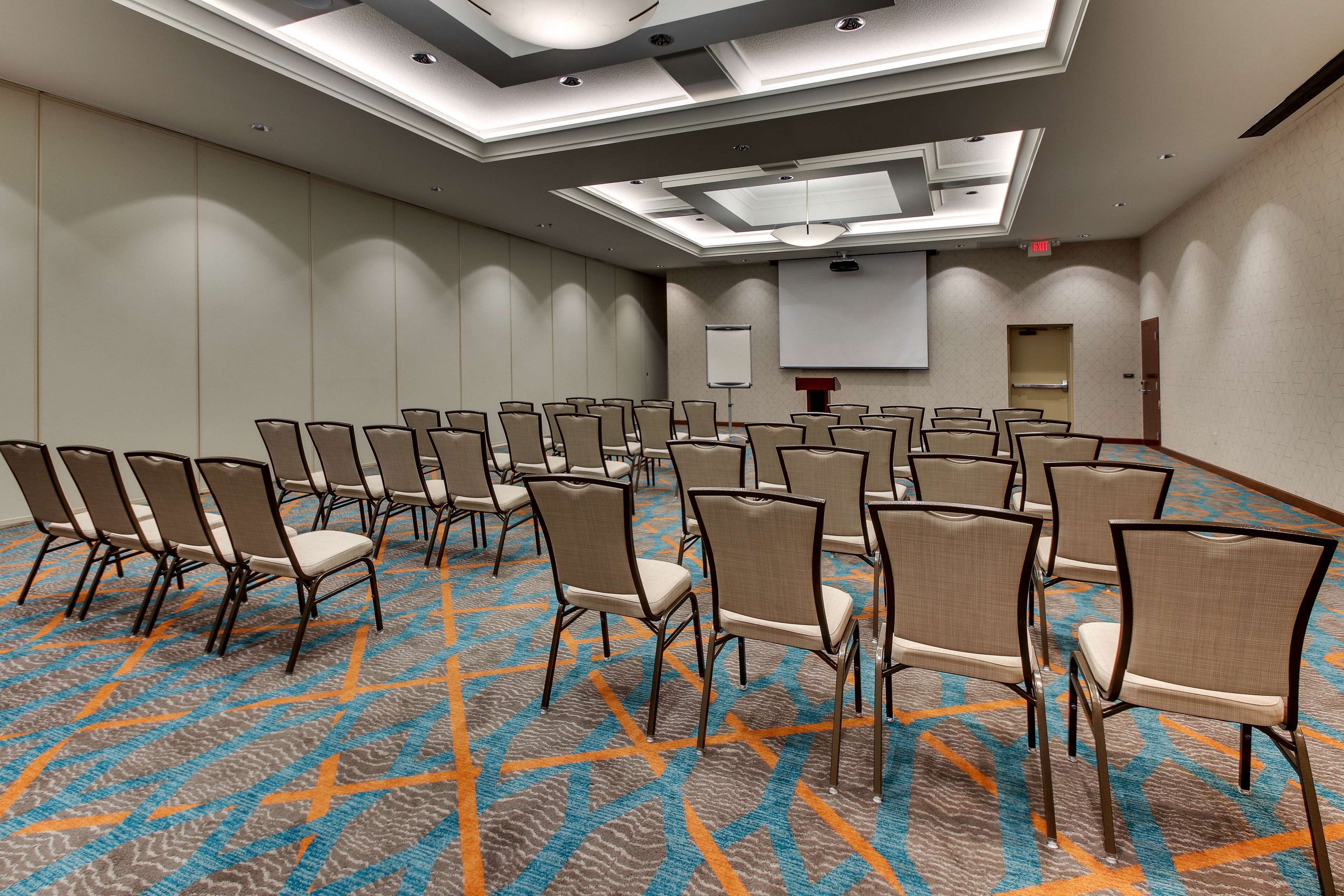 A conference room with rows of chairs, a projector screen, and a carpeted floor.