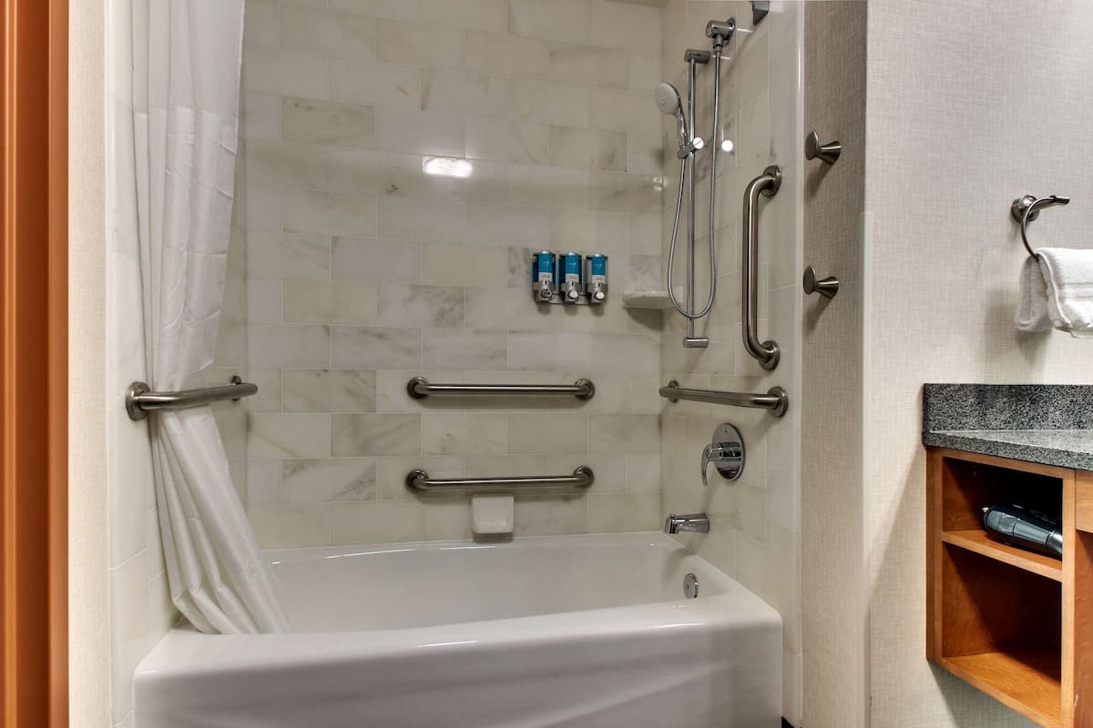 A modern bathroom with a bathtub, grab bars, a showerhead, and a soap dispenser.