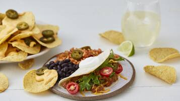 Un plato de nachos, un taco con ingredientes y un vaso de bebida blanca sobre una superficie blanca.