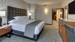 Habitación de hotel con una cama grande, una mesita de noche con lámpara, un aparador con espejo y suelo alfombrado.