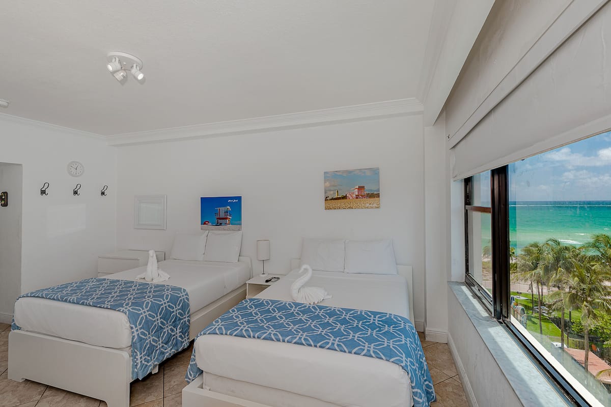 A hotel room with two beds, a view of the ocean, and a painting on the wall.