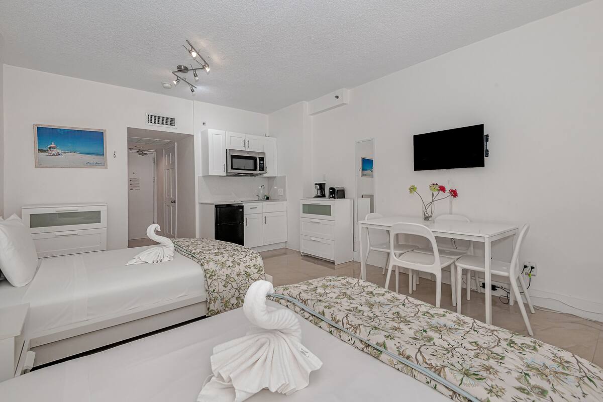 A hotel room with two beds, a kitchenette, a TV, and a dining area.