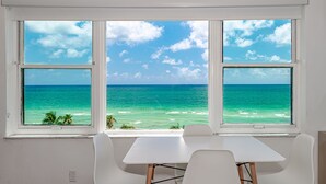 A room with a view of the ocean through three windows, a white table, and two white chairs. - Beach Front Studio (Miami Beach)