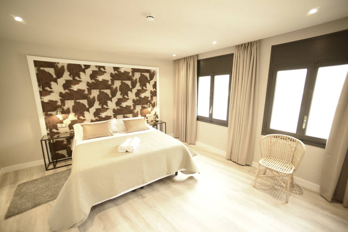 Un dormitorio con una cama grande, una silla, una mesita de noche y una pared con un diseño de hojas.