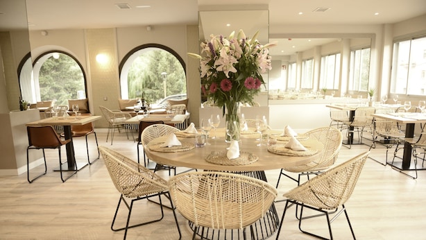 A dining area with round tables, wicker chairs, and a central floral arrangement.