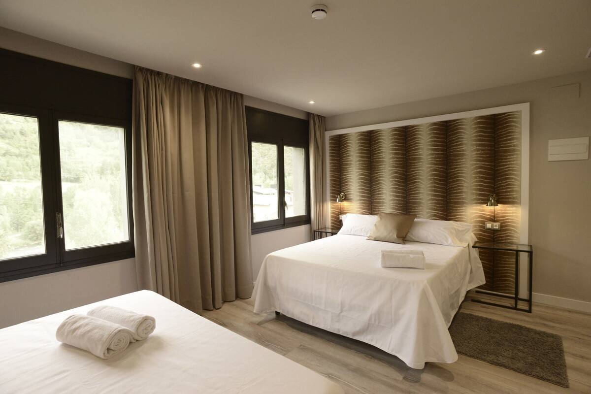 Un dormitorio moderno con una cama grande, una cama más pequeña y una mesita de noche con lámpara.